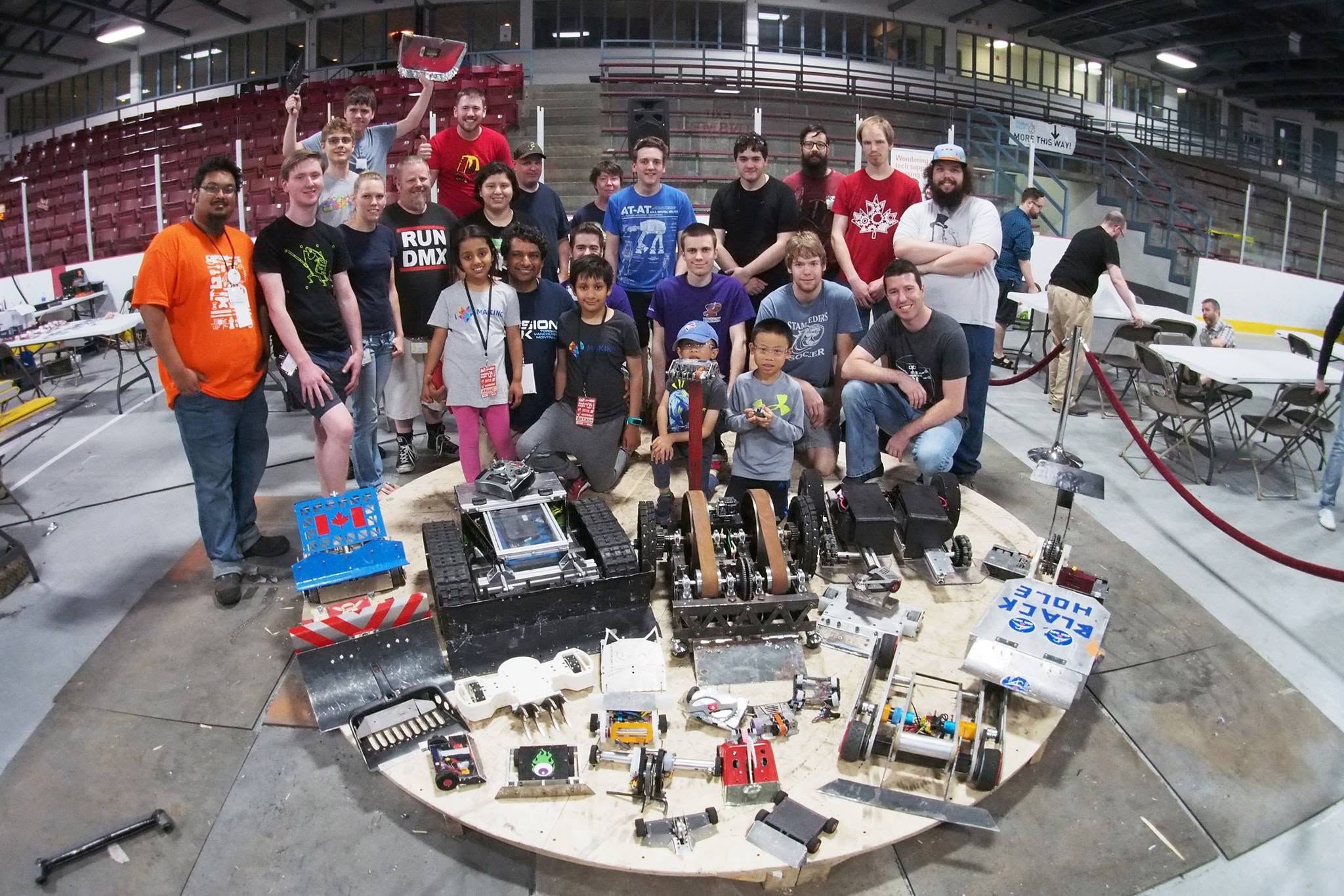 BotBrawl 2018 event group photo with 30+ participants surrounding combat robots on a circular arena